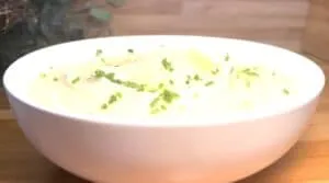 Creamy mashed potatoes in a white bowl topped with fresh chopped chives on a wooden table.
